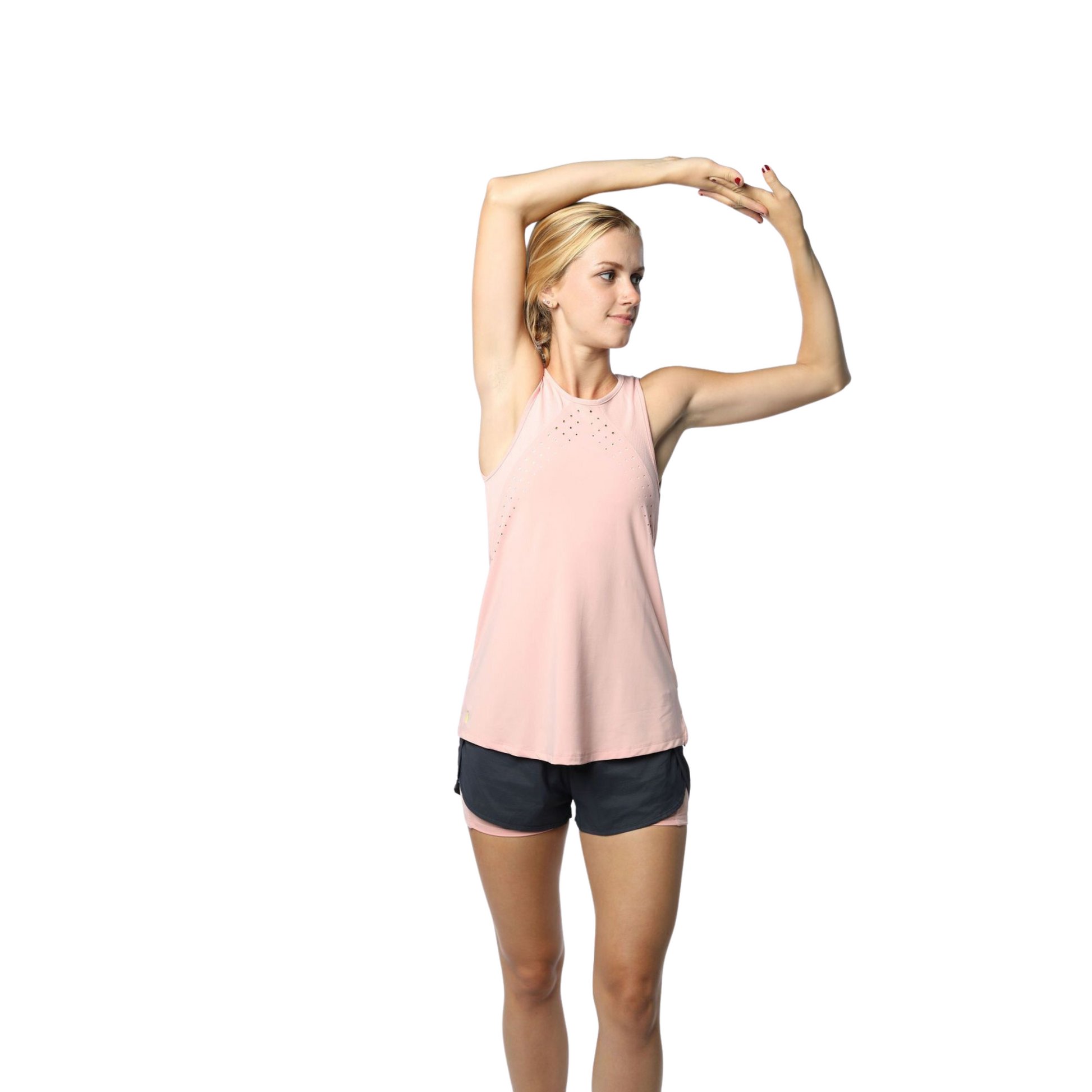 Woman wearing a blush pink athletic tank top and black shorts, arms stretched overhead. The tank features a laser-cut perforations, and mesh panels to increase breathability. The model demonstrate's the tank's comfortable fit and flexibility, perfect for any workout.