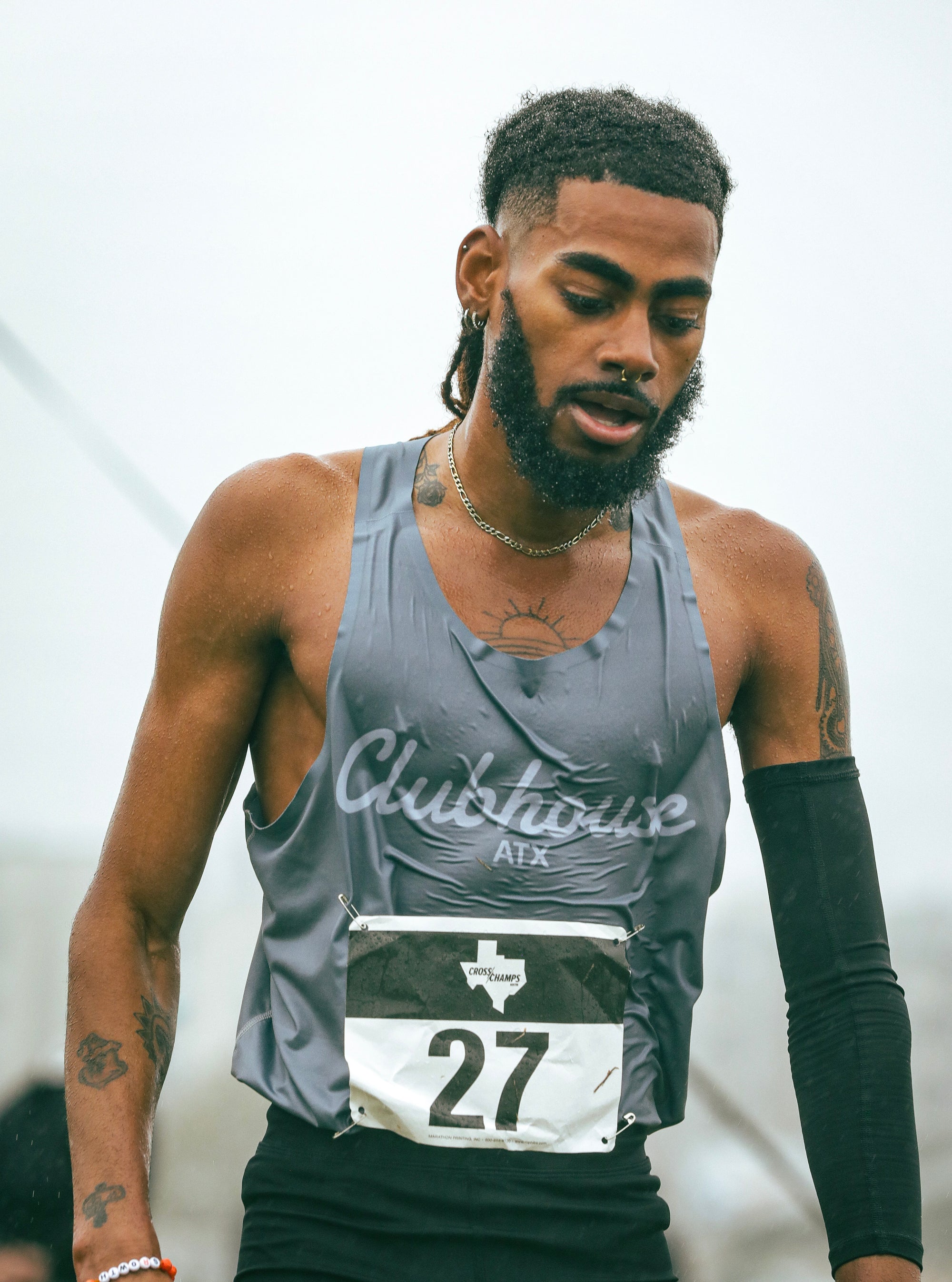 Black male running athlete representing Clubhouse Outfitters ATX during a race, man has a nose ring and multiple tattoos, and has a black sleeve on his left arm.