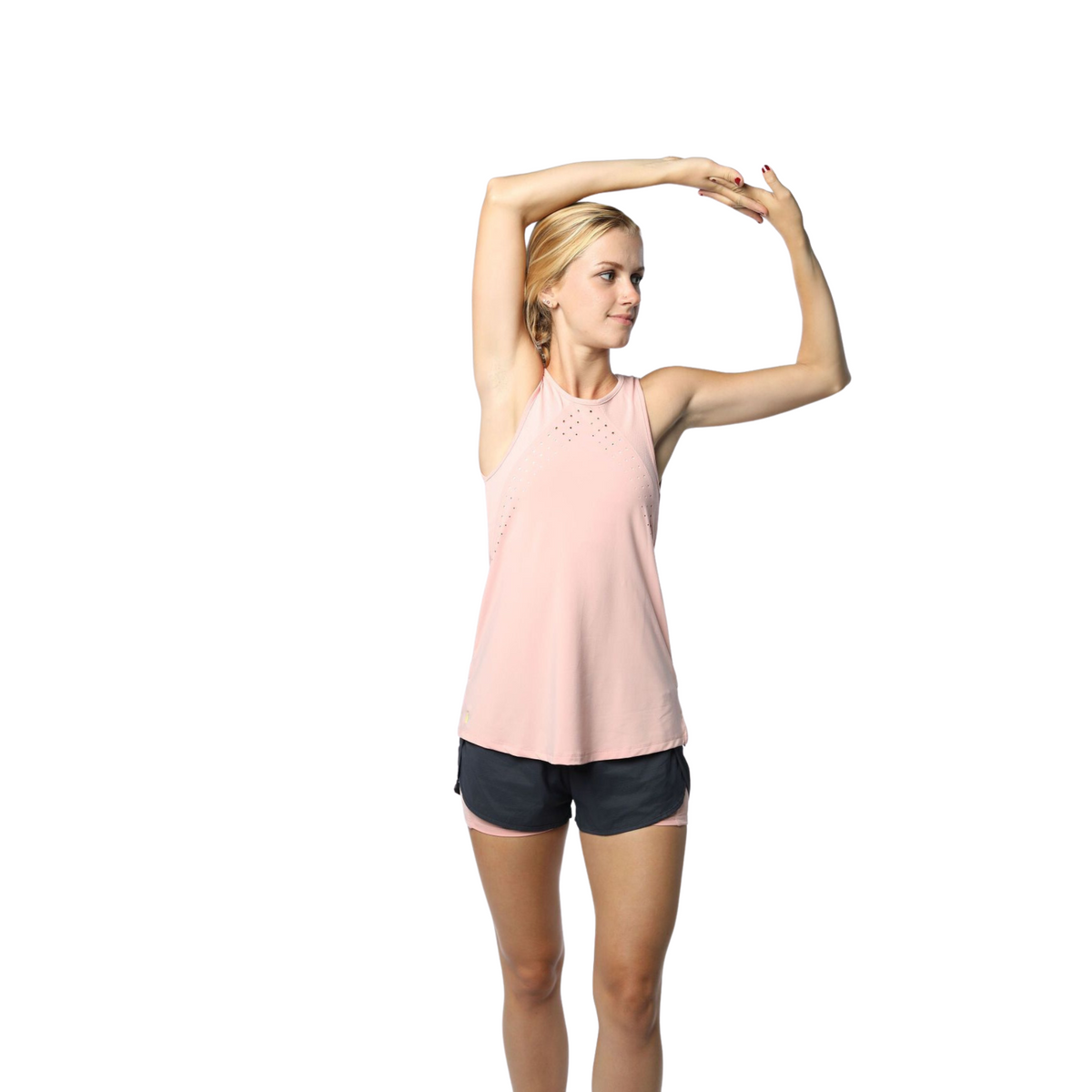 Woman wearing a blush pink athletic tank top and black shorts, arms stretched overhead. The tank features a laser-cut perforations, and mesh panels to increase breathability. The model demonstrate&#39;s the tank&#39;s comfortable fit and flexibility, perfect for any workout.